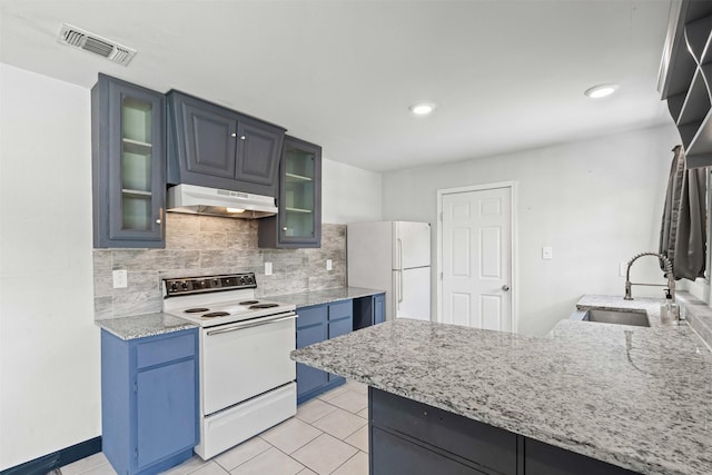 1212 E Mulkey St, Fort Worth, TX 76104 - kitchen with white appliances, blue cabinets, under cabinet range hood, light tile patterned floors, and tasteful backsplash