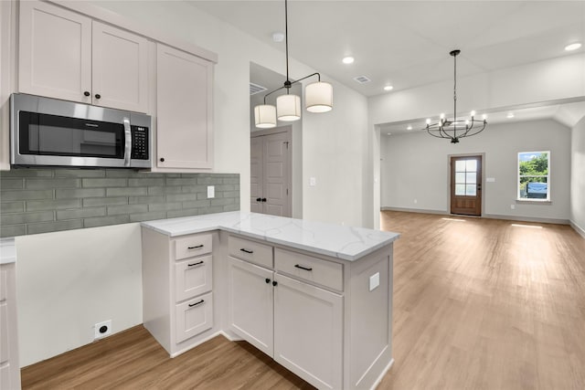 1604 Franklin St, Weatherford, TX 76086 - kitchen featuring stainless steel microwave, light wood-style flooring, open floor plan, light stone countertops, and decorative backsplash