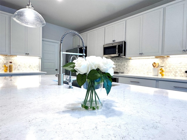 7204 Silent Mill Rd, Arlington, TX 76001 - kitchen with stainless steel microwave, backsplash, light stone countertops, decorative light fixtures, and white cabinetry