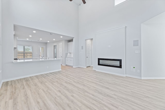 1957 Jade Forest Ln, Mesquite, TX 75181 - unfurnished living room featuring light wood-style floors, a ceiling fan, a glass covered fireplace, a towering ceiling, and recessed lighting
