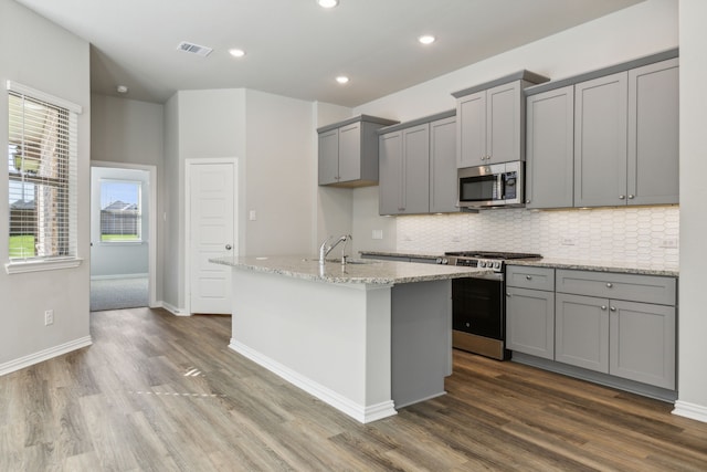 2021 Jade Frst, Mesquite, TX 75181 - kitchen featuring appliances with stainless steel finishes, gray cabinetry, dark wood-style floors, tasteful backsplash, and an island with sink
