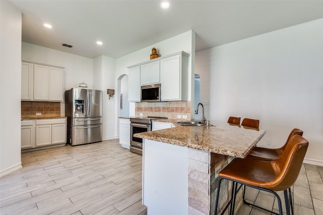 1015 Seider Ln, Grand Prairie, TX 75052 - kitchen with appliances with stainless steel finishes, decorative backsplash, a peninsula, a kitchen bar, and light stone countertops