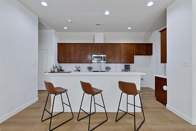 7064 Dreammaker Way, Frisco, TX 75035 - kitchen featuring stainless steel microwave, a breakfast bar area, light wood-type flooring, light countertops, and recessed lighting