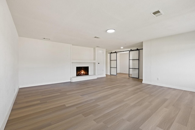719 Sara Dr, Mesquite, TX 75149 - unfurnished living room featuring a barn door, light wood-style flooring, and a fireplace