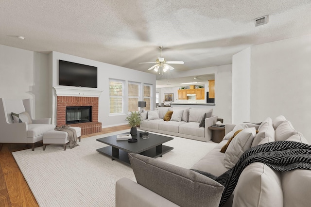 808 Elbe Dr, Arlington, TX 76001 - living area with a textured ceiling, wood finished floors, a ceiling fan, and a brick fireplace