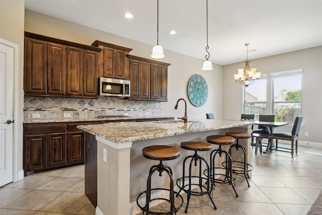 5009 Thistle Hl, Denton, TX 76210 - kitchen featuring stainless steel appliances, decorative backsplash, light tile patterned floors, a chandelier, and a kitchen island with sink