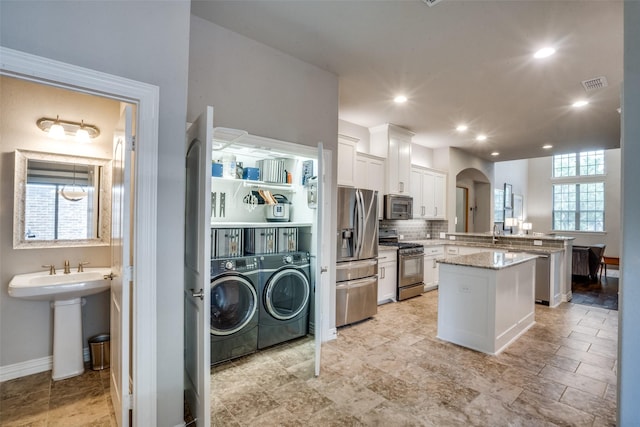 655 Emily Ln, Richardson, TX 75081 - kitchen featuring stainless steel appliances, washing machine and clothes dryer, a peninsula, arched walkways, and a center island