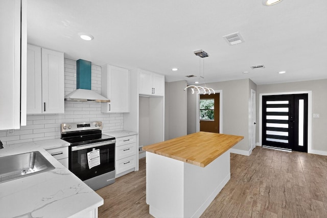 5612 Meadow Nest Dr, Dallas, TX 75236 - kitchen with stainless steel electric range oven, wall chimney exhaust hood, butcher block countertops, white cabinetry, and light wood-style flooring