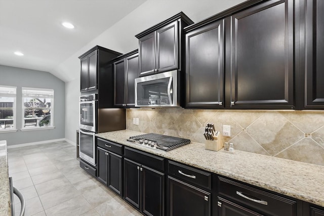 1129 Berrydale Dr, Northlake, TX 76226 - kitchen featuring appliances with stainless steel finishes, decorative backsplash, dark cabinets, vaulted ceiling, and light stone countertops