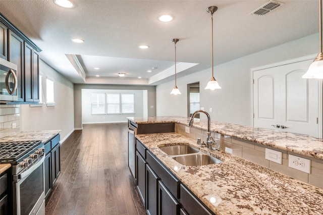 2111 Bentwater Ln, Frisco, TX 75036 - kitchen with stainless steel appliances, dark wood-style floors, decorative light fixtures, a raised ceiling, and light stone counters