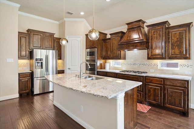 632 Fishback Cir, Plano, TX 75074 - kitchen with stainless steel appliances, custom range hood, dark wood finished floors, a center island with sink, and crown molding