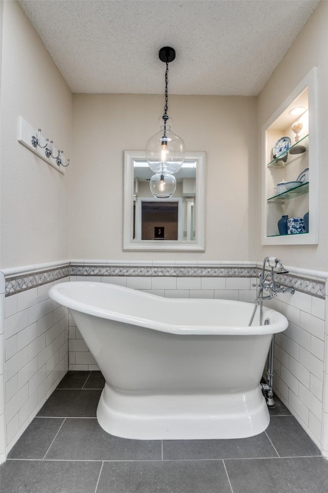 5205 Shady Springs Ct, Arlington, TX 76017 - bathroom featuring tile walls, wainscoting, a freestanding bath, tile patterned flooring, and a textured ceiling