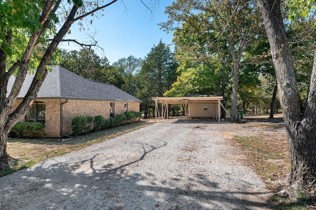 143 Shady Woods Ln, Denison, TX 75021 - view of home's exterior featuring a shingled roof, gravel driveway, brick siding, and a detached carport