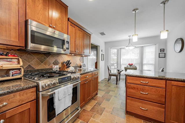 325 Los Santos Dr, Garland, TX 75043 - kitchen featuring appliances with stainless steel finishes, decorative backsplash, stone finish flooring, brown cabinetry, and pendant lighting