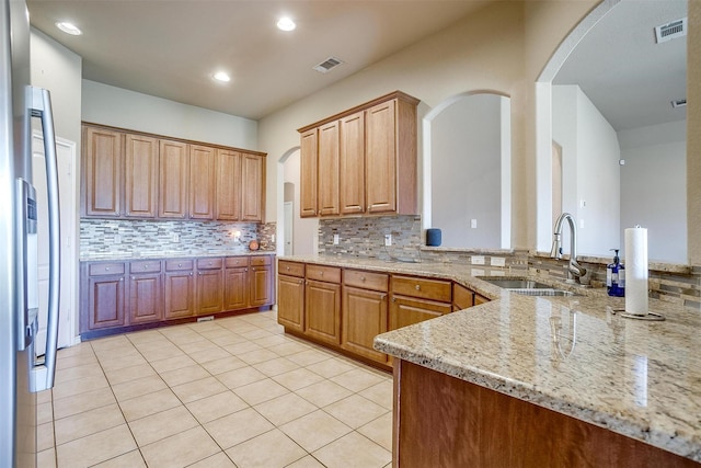 1201 Claire Ct, Burleson, TX 76028 - kitchen featuring decorative backsplash, light stone counters, arched walkways, light tile patterned floors, and a peninsula
