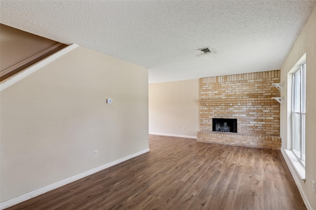 6569 Westridge Dr, Watauga, TX 76148 - unfurnished living room featuring wood finished floors, a textured ceiling, a brick fireplace, and healthy amount of natural light