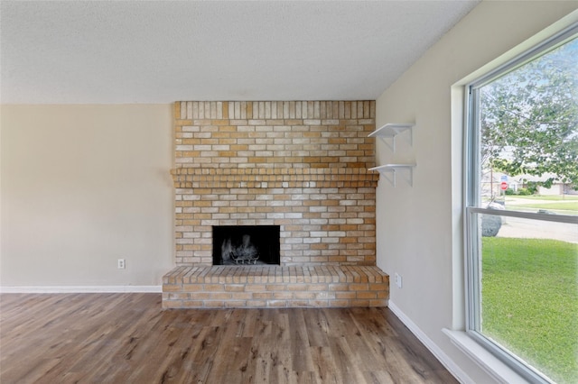 6569 Westridge Dr, Watauga, TX 76148 - unfurnished living room featuring a brick fireplace, wood finished floors, plenty of natural light, and a textured ceiling