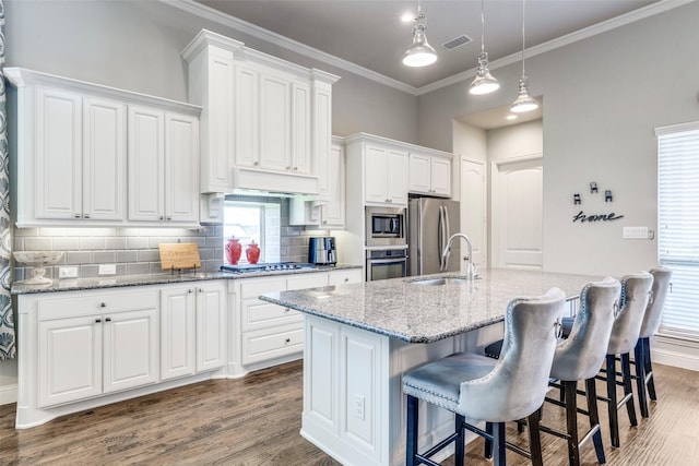 3300 Western Bluff Ct, Mansfield, TX 76063 - kitchen featuring appliances with stainless steel finishes, wood finished floors, a center island with sink, decorative backsplash, and white cabinets