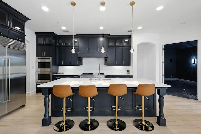 320 W Highland St, Southlake, TX 76092 - kitchen featuring appliances with stainless steel finishes, arched walkways, light countertops, backsplash, and light wood-style floors