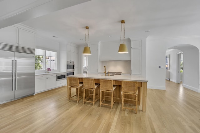 6819 Park Ln, Dallas, TX 75225 - kitchen featuring built in appliances, arched walkways, light wood-style floors, white cabinets, and light countertops