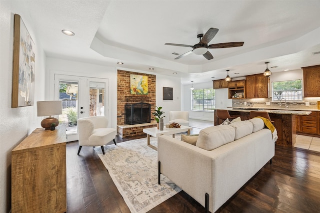 321 Malero Dr, Grand Prairie, TX 75051 - living room featuring a raised ceiling, a brick fireplace, a ceiling fan, recessed lighting, and dark wood-style floors