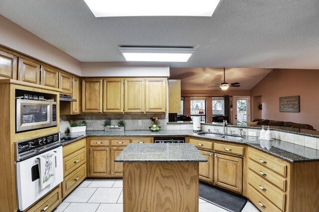 3008 Stone Bluff Ct, Arlington, TX 76017 - kitchen with oven, stainless steel microwave, a peninsula, dark stone countertops, and under cabinet range hood