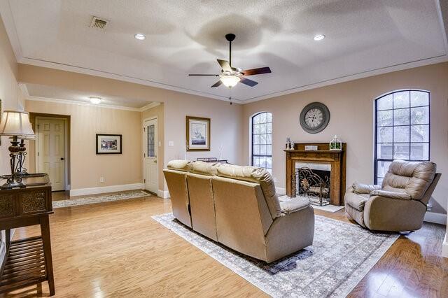 3008 Stone Bluff Ct, Arlington, TX 76017 - living area with ceiling fan, light wood-type flooring, crown molding, a tray ceiling, and a fireplace with flush hearth