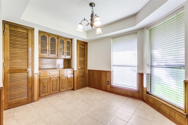 2307 Silver Holly Ln, Richardson, TX 75082 - unfurnished dining area featuring a raised ceiling, a chandelier, a textured ceiling, wainscoting, and light tile patterned flooring