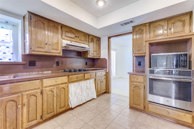 2307 Silver Holly Ln, Richardson, TX 75082 - kitchen featuring appliances with stainless steel finishes, under cabinet range hood, light tile patterned floors, and brown cabinetry