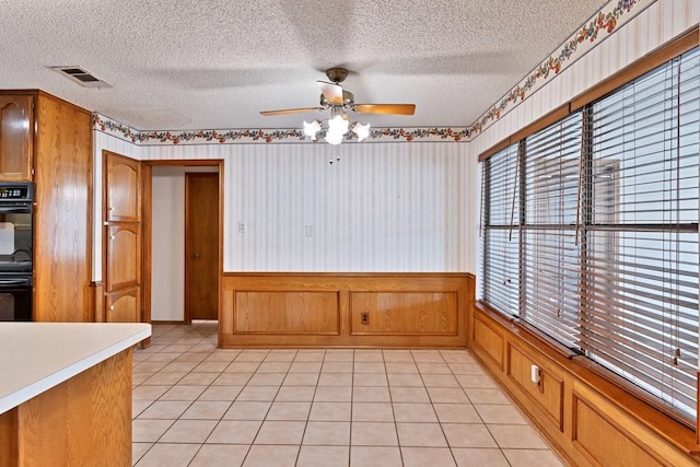 7254 Hialeah Cir W, North Richland Hills, TX 76182 - unfurnished dining area with a textured ceiling, a ceiling fan, a wainscoted wall, light tile patterned flooring, and wallpapered walls
