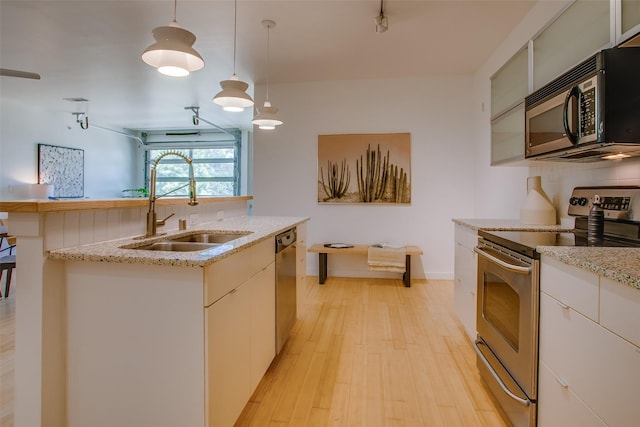 1111 S Akard St Unit 310, Dallas, TX 75215 - kitchen featuring appliances with stainless steel finishes, light wood finished floors, decorative light fixtures, light stone counters, and a kitchen island with sink