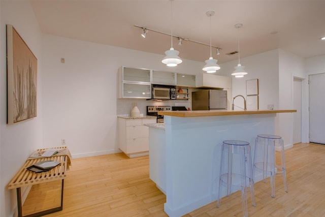 1111 S Akard St Unit 310, Dallas, TX 75215 - kitchen featuring appliances with stainless steel finishes, track lighting, light wood-style floors, white cabinets, and a kitchen bar