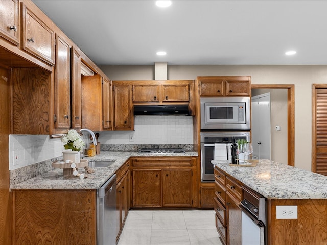 4108 Grand Lake Dr, Lake Worth, TX 76135 - kitchen with appliances with stainless steel finishes, under cabinet range hood, backsplash, brown cabinetry, and light stone counters