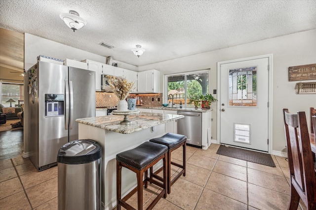 4201 Ravenhill Ln, Arlington, TX 76016 - kitchen featuring stainless steel appliances, white cabinetry, a kitchen island, a textured ceiling, and light tile patterned floors