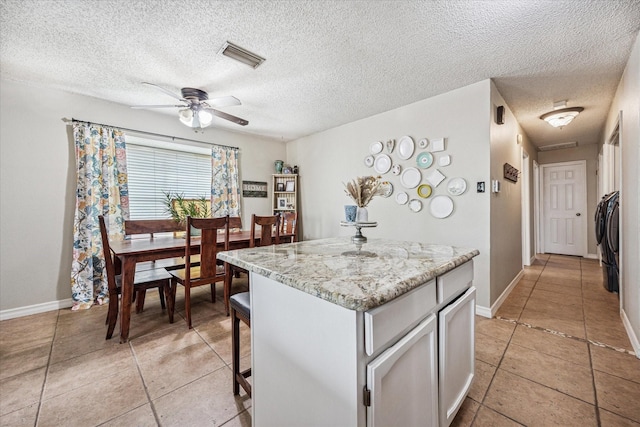 4201 Ravenhill Ln, Arlington, TX 76016 - kitchen featuring light tile patterned floors, a ceiling fan, a center island, a textured ceiling, and light stone counters