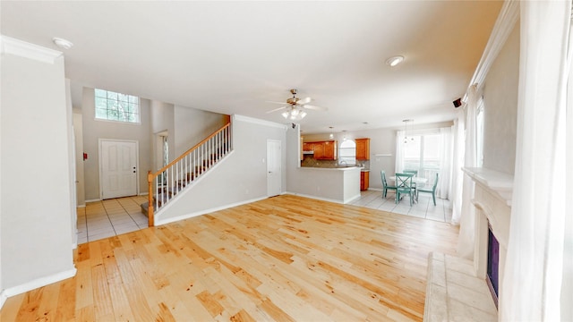 4009 Bickmore Ln, Fort Worth, TX 76244 - unfurnished living room with stairs, ceiling fan, light wood finished floors, a fireplace with raised hearth, and ornamental molding
