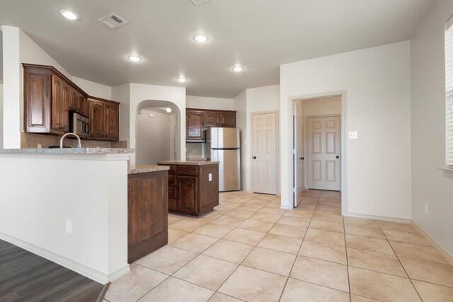 3228 Buckthorn Ln, Denton, TX 76226 - kitchen featuring freestanding refrigerator, stainless steel microwave, arched walkways, backsplash, and light tile patterned floors