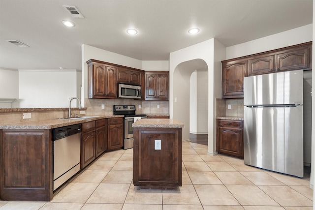 3228 Buckthorn Ln, Denton, TX 76226 - kitchen featuring appliances with stainless steel finishes, arched walkways, a kitchen island, tasteful backsplash, and recessed lighting
