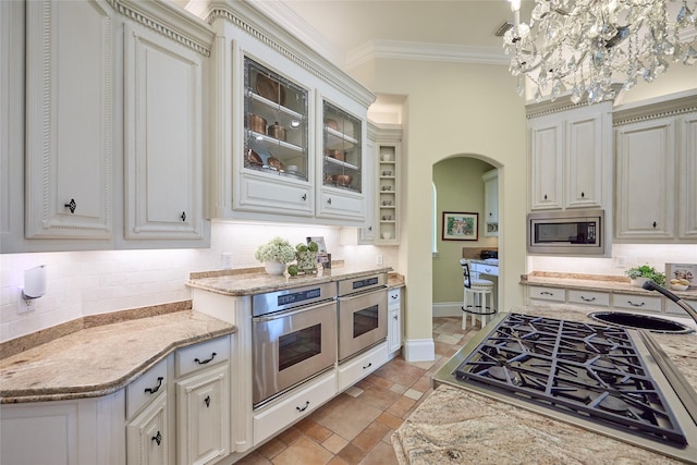 5 Savannah Ridge Dr, Frisco, TX 75034 - kitchen with stainless steel appliances, arched walkways, tasteful backsplash, crown molding, and glass insert cabinets