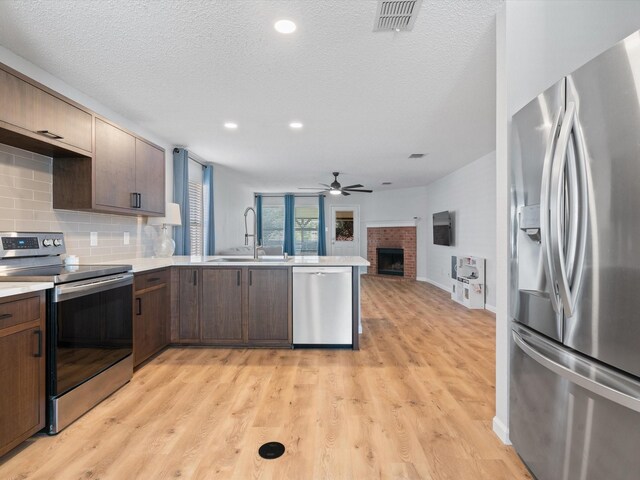 1545 Knottingham Dr, Little Elm, TX 75068 - kitchen with stainless steel appliances, a peninsula, a ceiling fan, light countertops, and a fireplace