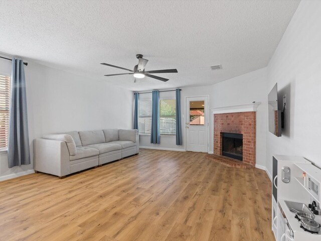 1545 Knottingham Dr, Little Elm, TX 75068 - living area featuring a textured ceiling, ceiling fan, light wood finished floors, and a brick fireplace