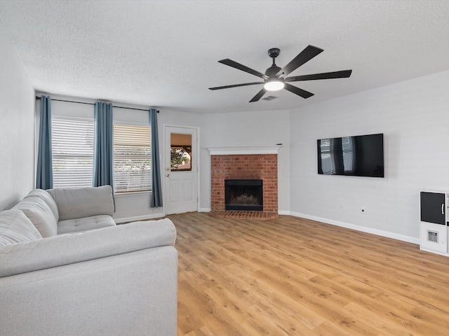 1545 Knottingham Dr, Little Elm, TX 75068 - living room with a textured ceiling, light wood-style flooring, a ceiling fan, and a brick fireplace