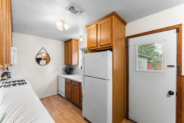 1238 Caladium Dr, Mesquite, TX 75149 - kitchen with white appliances, light countertops, light wood finished floors, brown cabinetry, and a textured ceiling