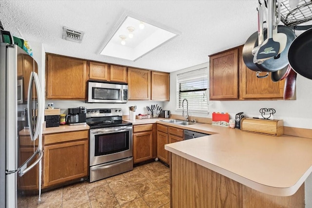 4900 Highbank Dr, Arlington, TX 76018 - kitchen featuring stainless steel appliances, a peninsula, brown cabinetry, a skylight, and a textured ceiling