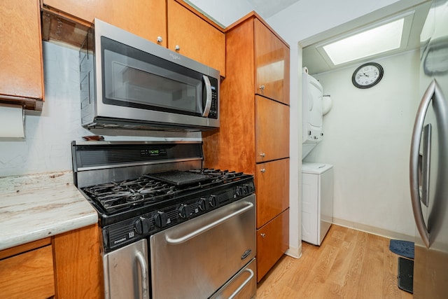 514 Fairview Dr, Richardson, TX 75081 - kitchen with appliances with stainless steel finishes, estacked washer and dryer, light wood-style floors, and brown cabinets