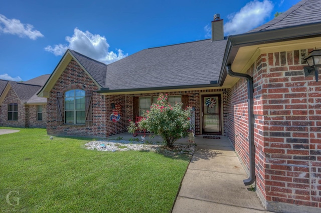 189 Bent Tree Loop, Haughton, LA 71037 - view of exterior entry featuring brick siding, a shingled roof, a chimney, and a lawn