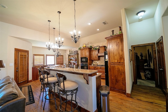 1702 High Point Dr, Pilot Point, TX 76258 - kitchen with black appliances, a chandelier, brown cabinetry, a kitchen breakfast bar, and an island with sink