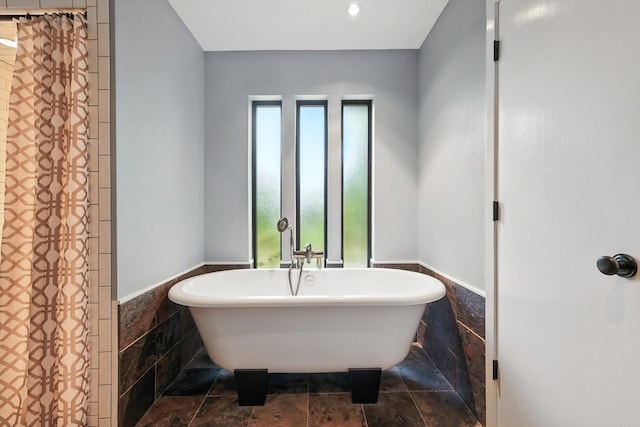 9901 Burnham Dr, Dallas, TX 75243 - full bath featuring wainscoting, tile walls, a soaking tub, and stone finish floors