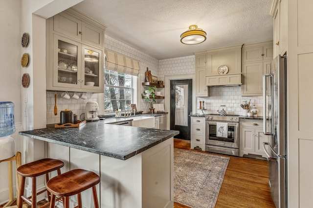 887 N Clinton St, Stephenville, TX 76401 - kitchen with high quality appliances, a peninsula, a textured ceiling, decorative backsplash, and dark countertops