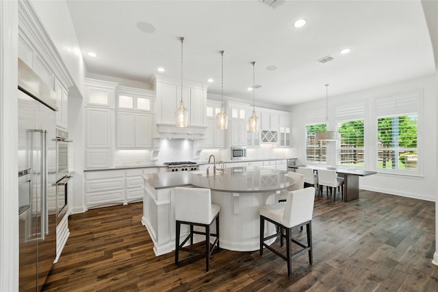 4510 Woodbine Ln, Prosper, TX 75078 - kitchen with decorative backsplash, an island with sink, dark wood-type flooring, a kitchen bar, and white cabinetry